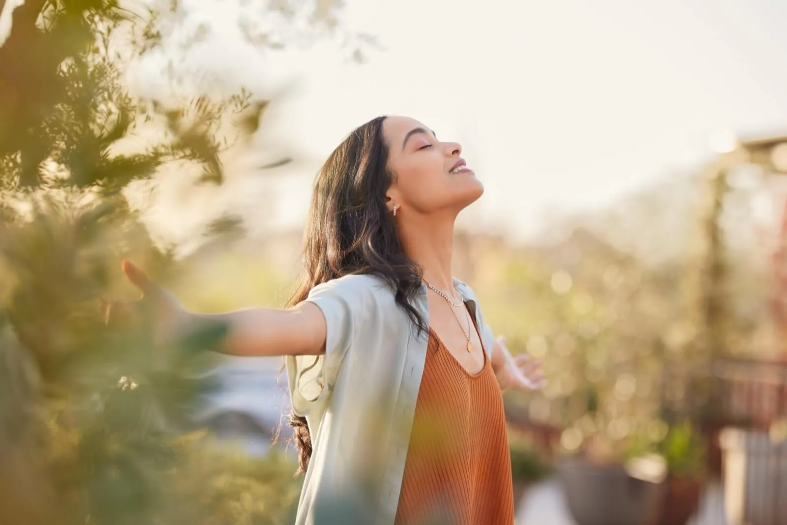 Person in orange dress enjoying nature with arms outstretched in golden sunlight